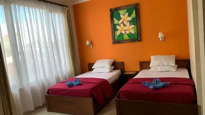 two beds in a room with orange walls at Taxa Uma Guest House in Kuta