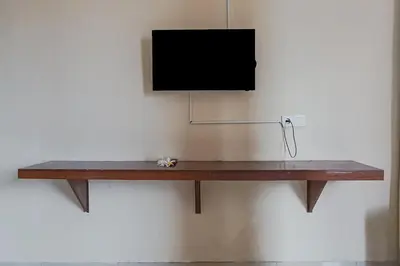 a television hanging on a wall with a wooden shelf at Taxa Uma Guest House in Kuta