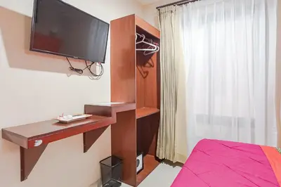a bedroom with a desk and a television on a wall at Taxa Uma Guest House in Kuta
