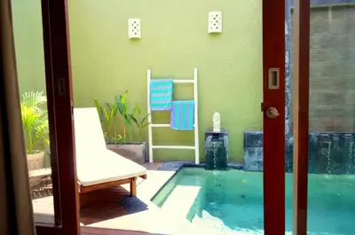 a swimming pool with a chair next to a house at Jas Green Villas and Spa in Seminyak