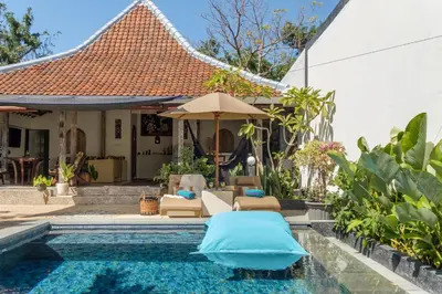 a pool with chairs and an umbrella next to a house at Madeira Javanese Joglo, Jimbaran in Jimbaran