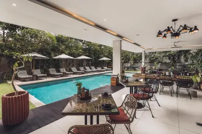 an outdoor patio with tables and chairs and a swimming pool at Monolocale Resort & Spa Seminyak by Ini Vie Hospitality in Seminyak