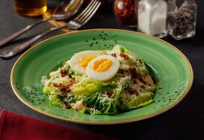 a green plate with a salad with eggs on it at Monolocale Resort & Spa Seminyak by Ini Vie Hospitality in Seminyak