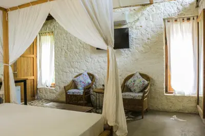 a bedroom with a bed and two chairs and a window at Chanteak Bali - Stone House 2 in Jimbaran