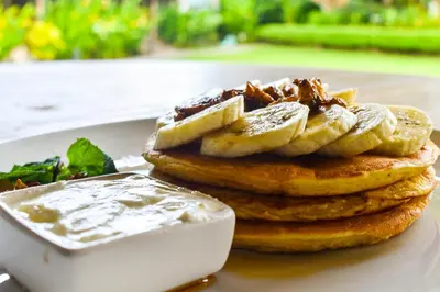 a stack of pancakes with bananas and a bowl of sauce at Chanteak Bali - Teak House 2 in Jimbaran