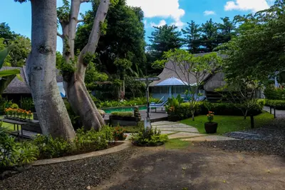 a garden with trees and a house in the background at Chanteak Bali - Teak House 2 in Jimbaran