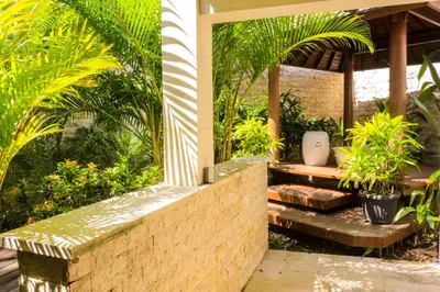 a garden with a bench and palm trees at Chanteak Bali - Teak House 2 in Jimbaran