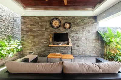 a living room with a couch and a tv on a brick wall at Simple And Magical . VILLA ALMAYA in Seminyak