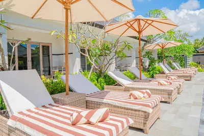 a row of lounge chairs with umbrellas on a patio at Green D'mel Bali in Nusa Dua