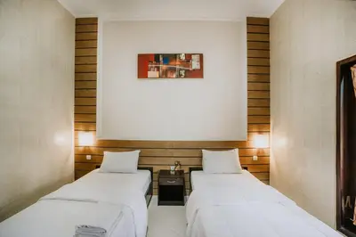 two beds in a room with a picture on the wall at DENAYS GUESTHOUSE JIMBARAN in Jimbaran