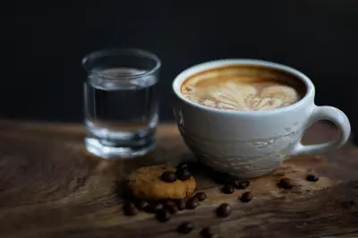 a cup of coffee and a cookie and a glass of water at Natya Hotel Kuta in Kuta