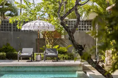 two chairs and an umbrella next to a pool at Villa Christie By Nakula in Seminyak