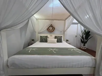 a bedroom with a canopy bed with white curtains at Tiga Pantai Villa Legian in Legian