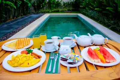 a table with plates of food next to a swimming pool at Delu Villas & Suite in Kerobokan