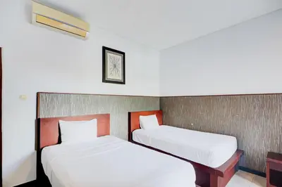 two beds in a hotel room with white sheets at Collection O Bali near Kedonganan Beach formerly New Asta Graha Homestay in Jimbaran