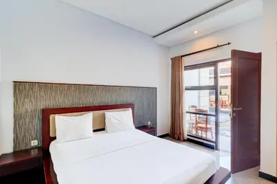 a bedroom with a white bed and a balcony at Collection O Bali near Kedonganan Beach formerly New Asta Graha Homestay in Jimbaran