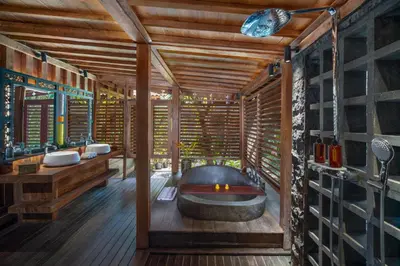 a bathroom with a tub in a room with wooden walls at Villa Kapungkur in Jimbaran