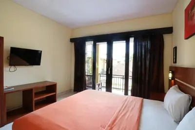 a bedroom with a bed and a television and a balcony at Kondra Premiere Guest House Kuta in Kuta