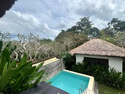 a swimming pool in a resort with a thatch roof at Mai Villa in Jimbaran