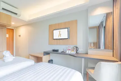 a room with a bed and a desk and a mirror at Horison Le Aman Bali in Jimbaran
