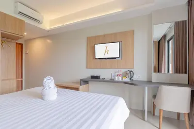 a bedroom with a white bed and a kitchen at Horison Le Aman Bali in Jimbaran