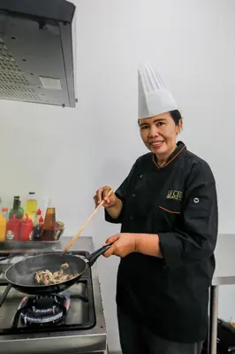 a woman in a chefs hat cooking food in a wok at Le Cielo Romantic Villas by Maviba in Seminyak