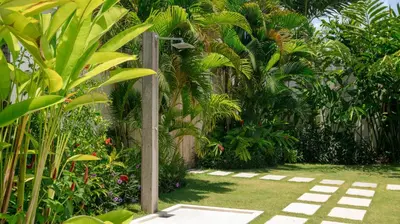 a garden with palm trees and a fence at Villa Aloui by Villa Finder in Kerobokan