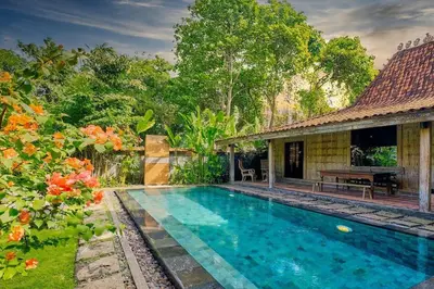 a swimming pool in front of a house with trees at Wahyu wonderful private honeymoon joglo in Seminyak