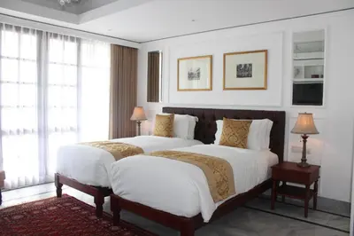 two beds in a bedroom with white walls and windows at The Colony Hotel Bali in Seminyak
