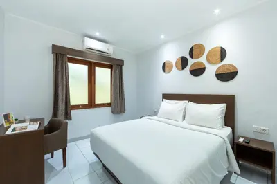 a hotel room with a bed and a desk and a window at Cove Matahari Guesthouse Sunset in Legian