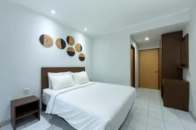 a bedroom with a large white bed and a small cabinet at Cove Matahari Guesthouse Sunset in Legian