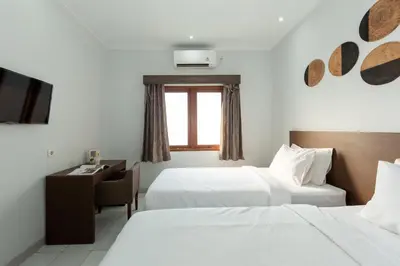 a hotel room with two beds and a desk and a television at Cove Matahari Guesthouse Sunset in Legian