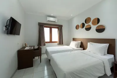 a hotel room with two beds and a television at Cove Matahari Guesthouse Sunset in Legian