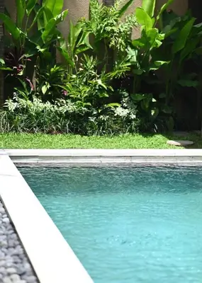 a swimming pool with blue water and green plants at Villa Searenity Seminyak in Seminyak