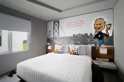 a bedroom with a large white bed with a poster on the wall at Berry Biz Hotel Sunset Road in Seminyak