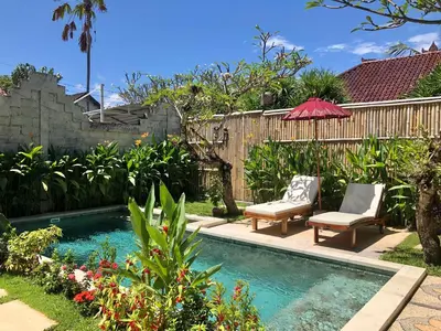 a backyard with a pool with two chairs and an umbrella at Villa Abhista Seminyak in Seminyak