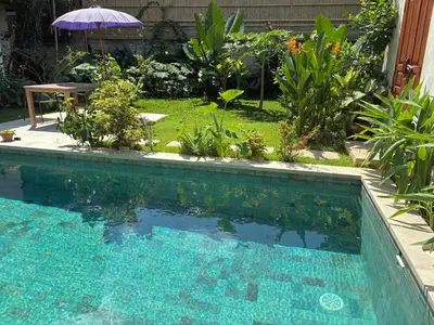 a swimming pool in a garden with a table and an umbrella at Villa Abhista Seminyak in Seminyak