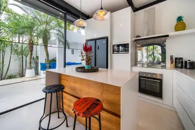 a kitchen with white counters and a wooden island with stools at Villa Vantage Canggu in Canggu
