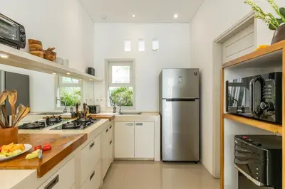 a kitchen with white cabinets and a stainless steel refrigerator at Fresh and Stylish 3bd Villa in Seminyak with Private Pool in Seminyak