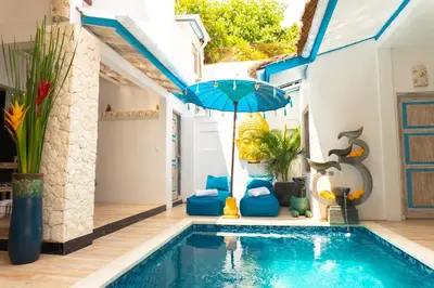 a swimming pool with a blue umbrella next to a house at Shray Villa. Legian in Legian
