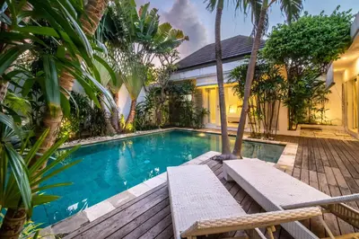a swimming pool in front of a house with trees at Villa Gallici Seminyak in Seminyak