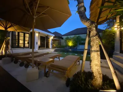 a patio with chairs and an umbrella next to a pool at Lotus Luxury Villa Seminyak in Seminyak