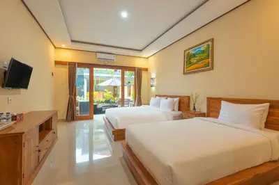 a hotel room with two beds and a television at Liliy Guest House Kuta in Legian