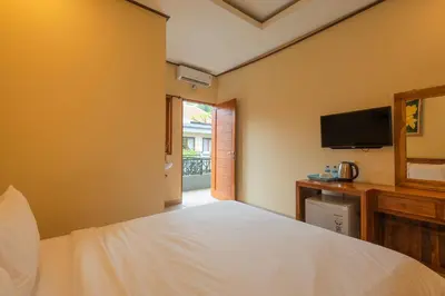 a bedroom with a white bed and a television at Liliy Guest House Kuta in Legian