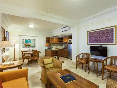 a living room with tables and chairs and a kitchen at Club Bali Suite Legian in Legian