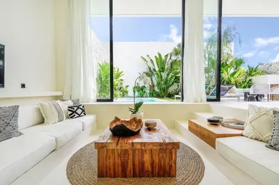 a living room with a wooden coffee table and large windows at Casa Umalas Villa by Betterplace in Canggu